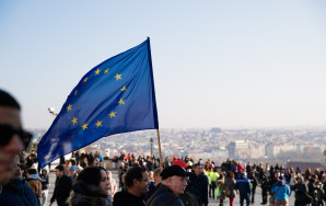 Bild einer Demonstration. Im Fokus steht eine EU Flagge, die im Wind weht